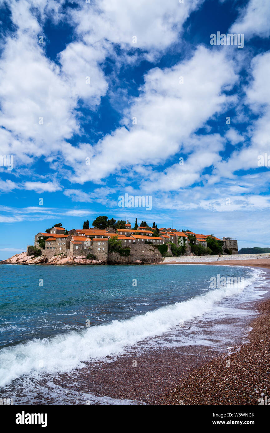 Montenegro, sulla spiaggia al famoso piccolo isolotto roccioso di Sveti Stefan con antiche case in pietra e tetti rossi in vacanza estiva Foto Stock