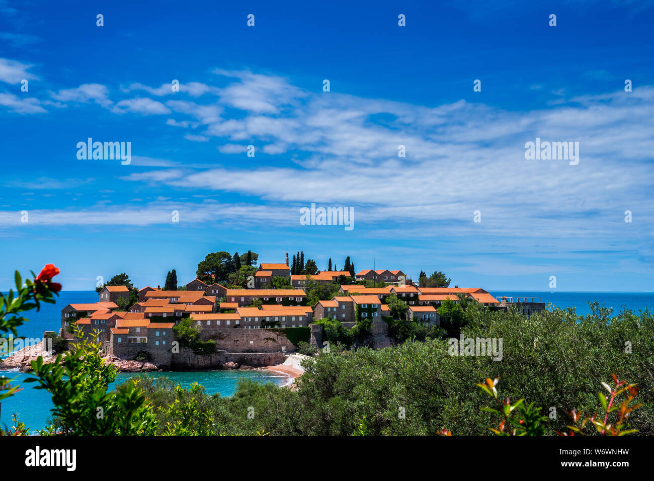 Montenegro, storiche case in pietra con il tetto rosso sull isolotto roccioso di Sveti Stefan in estate con il sole una perfetta destinazione per le vacanze Foto Stock