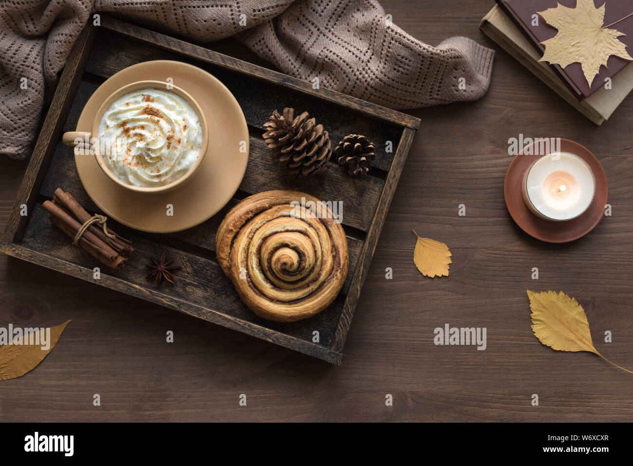 Casa accogliente e autunno hygge concetto. Stagionale composizione autunnale con soffici plaid, caffè latte, pasta fresca cannella bun, candela su legno, vista dall'alto Foto Stock
