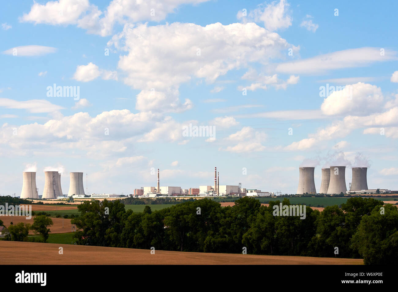 Vista dei comignoli fumanti di una centrale nucleare nel paesaggio con alberi e campi case sotto il cielo blu con nuvole. Foto Stock