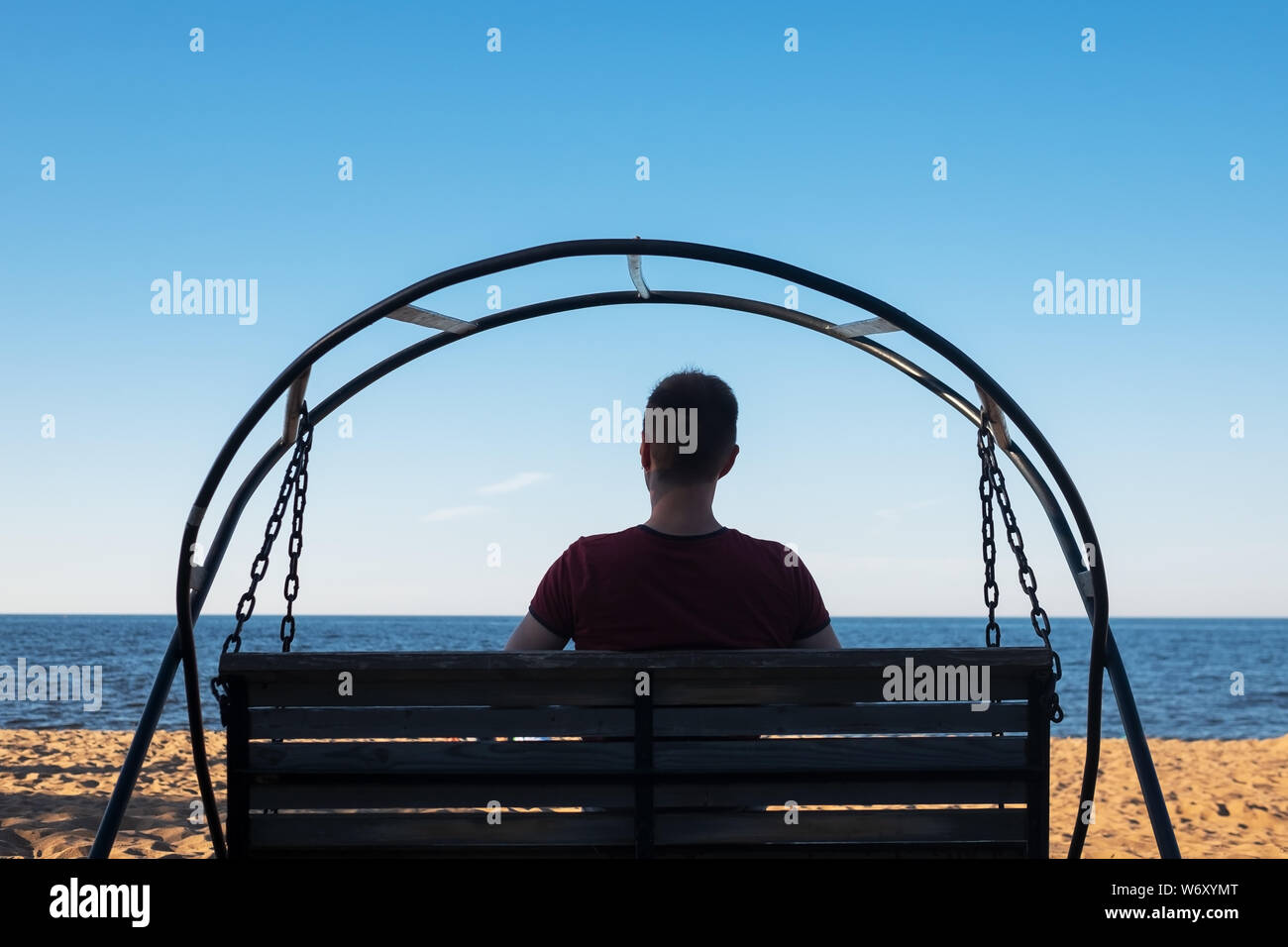 Uomo seduto su swing alla spiaggia sabbiosa e guardando il mare Foto Stock