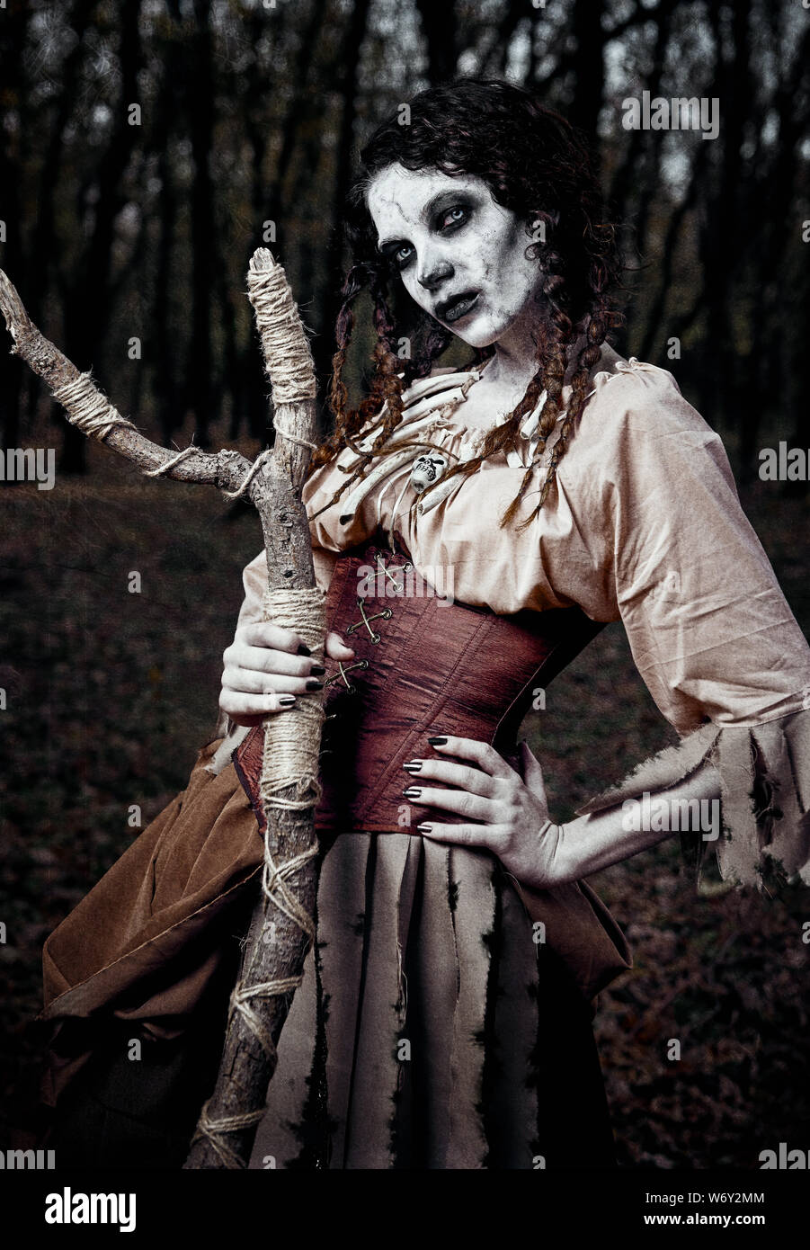 Tema Halloween: cupo creepy strega voodoo con bastone. Ritratto del perfido Hex nella foresta scura. Zombie donna (undead). Grunge effetto texture Foto Stock