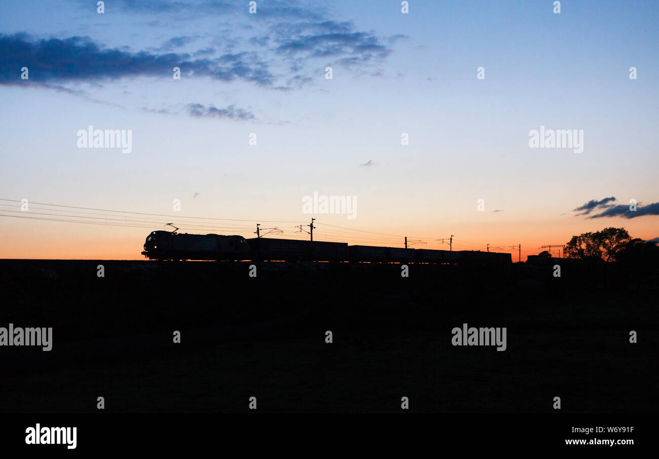 Direct Rail Services class 88 locomotore elettrico sulla costa ovest mainline facendo una silhouette al tramonto con la Stobart / Tesco treno merci Foto Stock