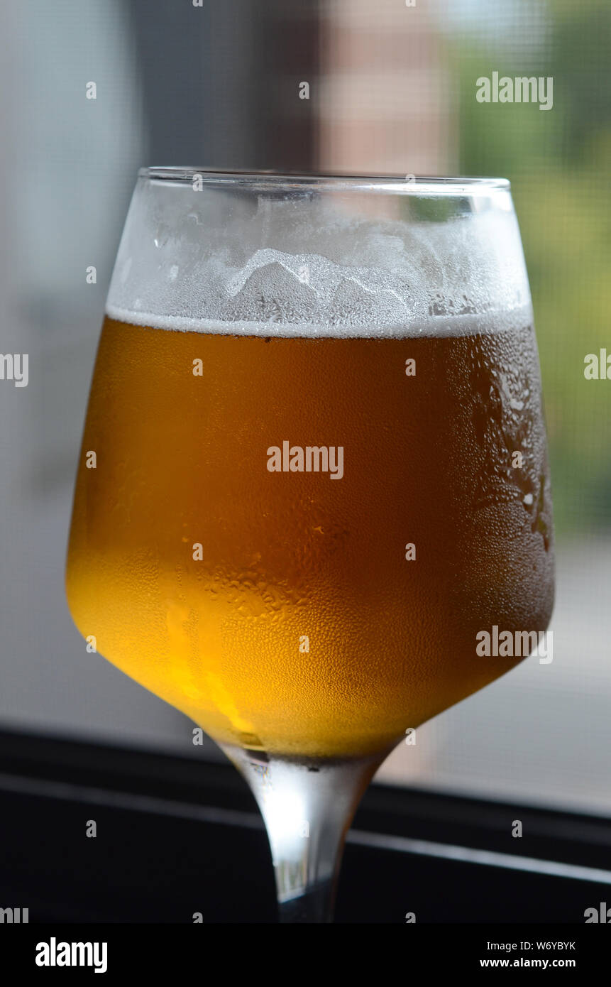 BREW HOUSE: Un primo piano di un bicchiere freddo di birra con acqua di condensazione che gocciola lateralmente e bolle gassate che si innalzano con una parte superiore gelida. Foto Stock