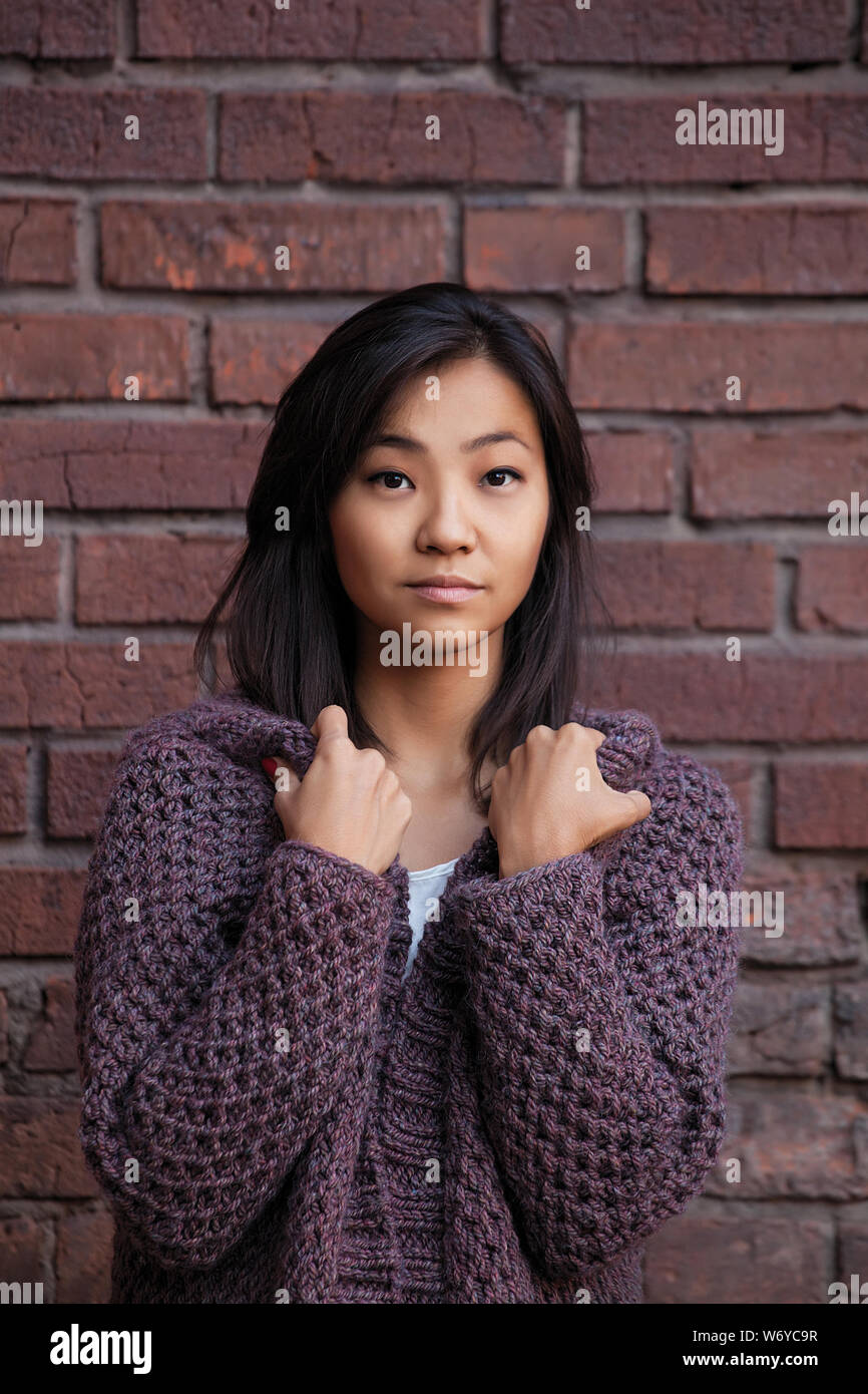 Bella asiatica giovane donna è in viola cardigan lavorato a maglia vicino a un muro di mattoni Foto Stock