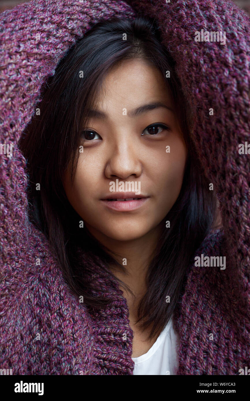 Bella asiatica giovane donna è in viola cardigan lavorato a maglia vicino a un muro di mattoni Foto Stock