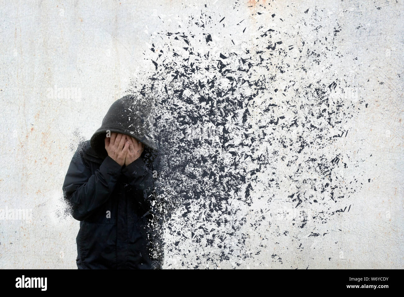 Una salute mentale concetto di un uomo incappucciato tenendo la testa tra le mani. Con il suo corpo disolving e si allontanano. Foto Stock