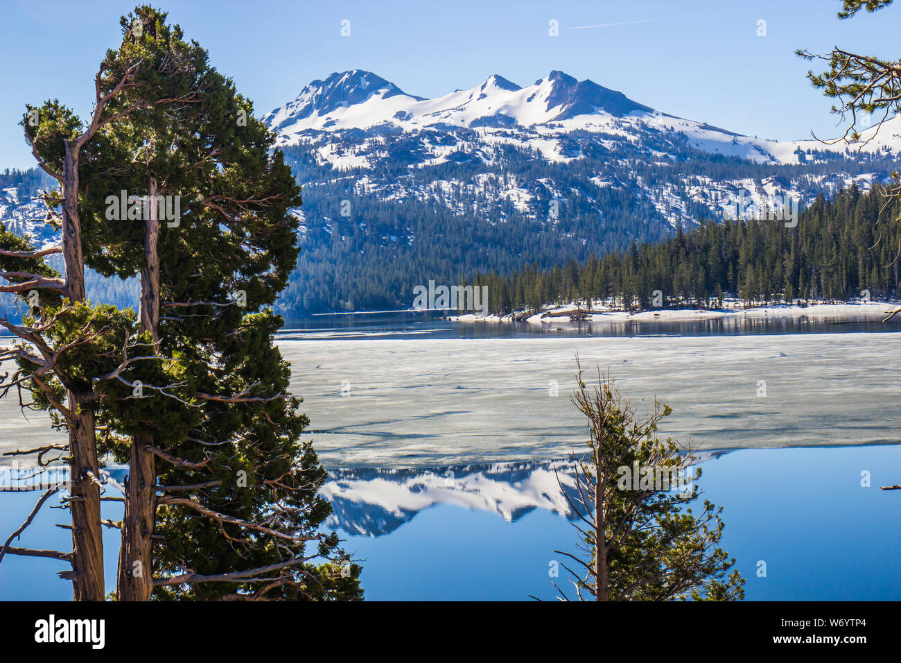 La riflessione di montagne coperte di neve su metà Lago Ghiacciato Foto Stock