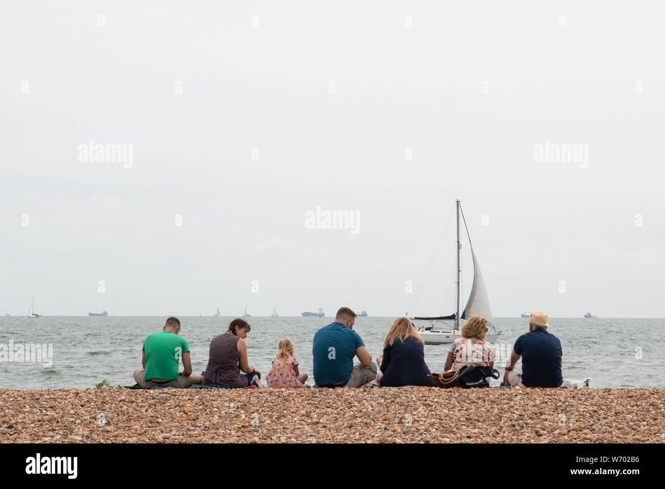 Una famiglia seduto su di una spiaggia di ciottoli presso il British seaside Foto Stock