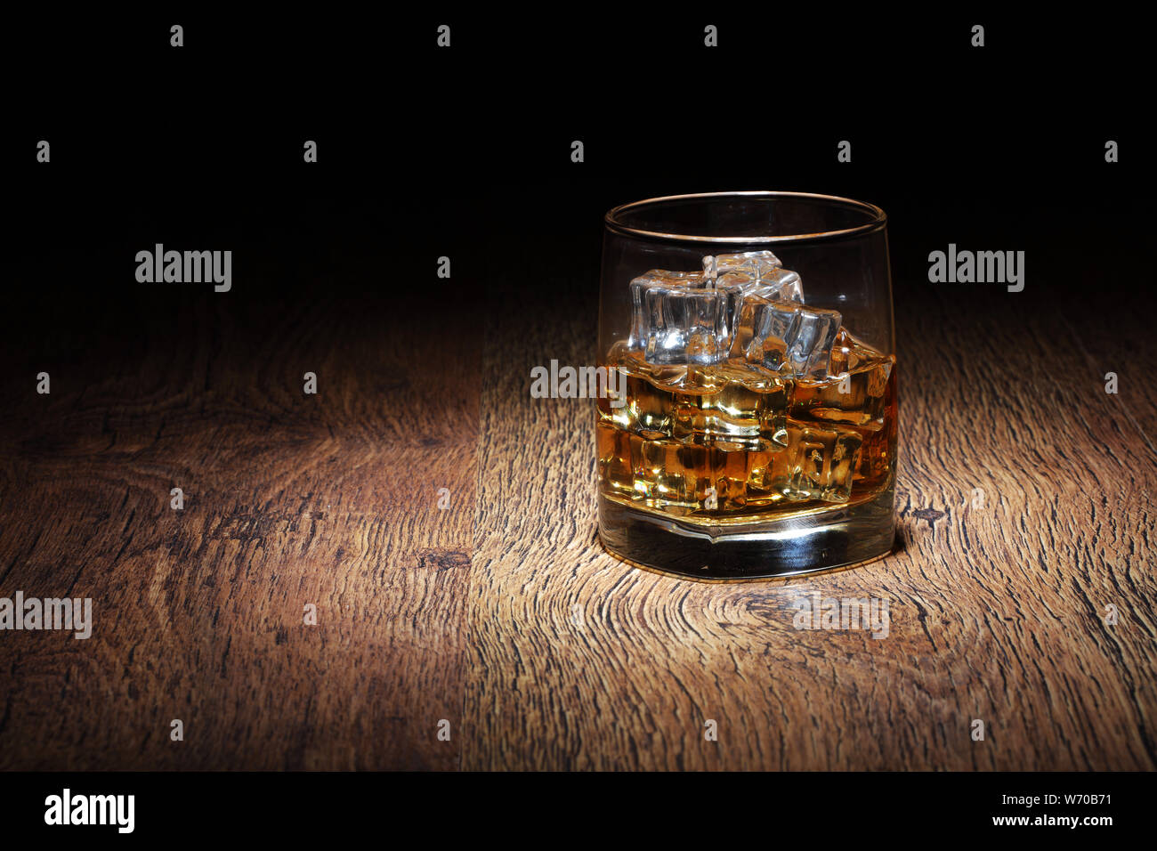 Un Scotch in un bicchiere di vetro con ghiaccio rocce sulla vecchia superficie di legno Foto Stock