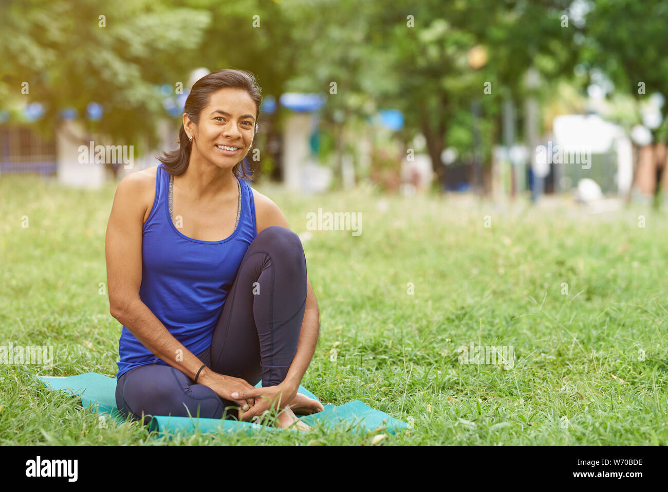 Sorridente giovane donna sportiva sedersi sul materassino yoga. Uno stile di vita sano in tema di città Foto Stock