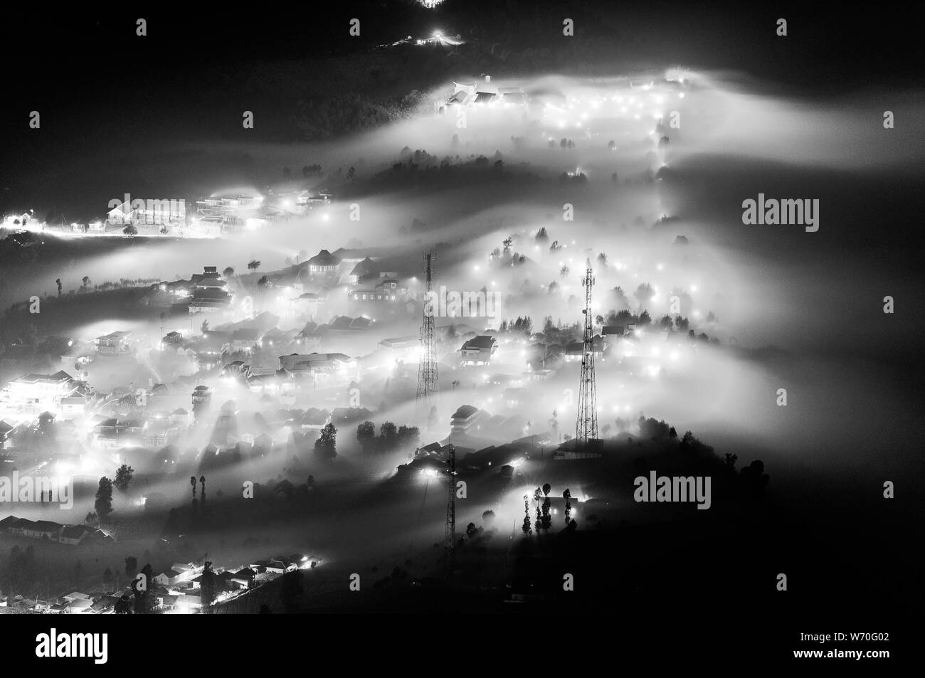 La nebbia che fluisce in un piccolo villaggio e gli alberi nei pressi del Monte Bromo di notte Foto Stock