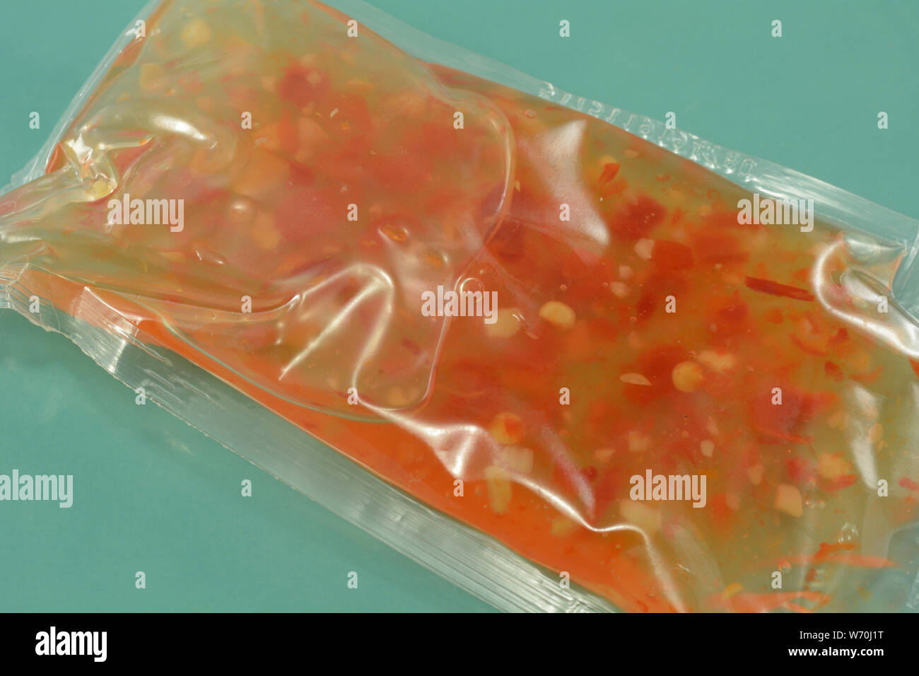 Close up di salsa al peperoncino dolce imballaggi in plastica sulla piastra blu Foto Stock