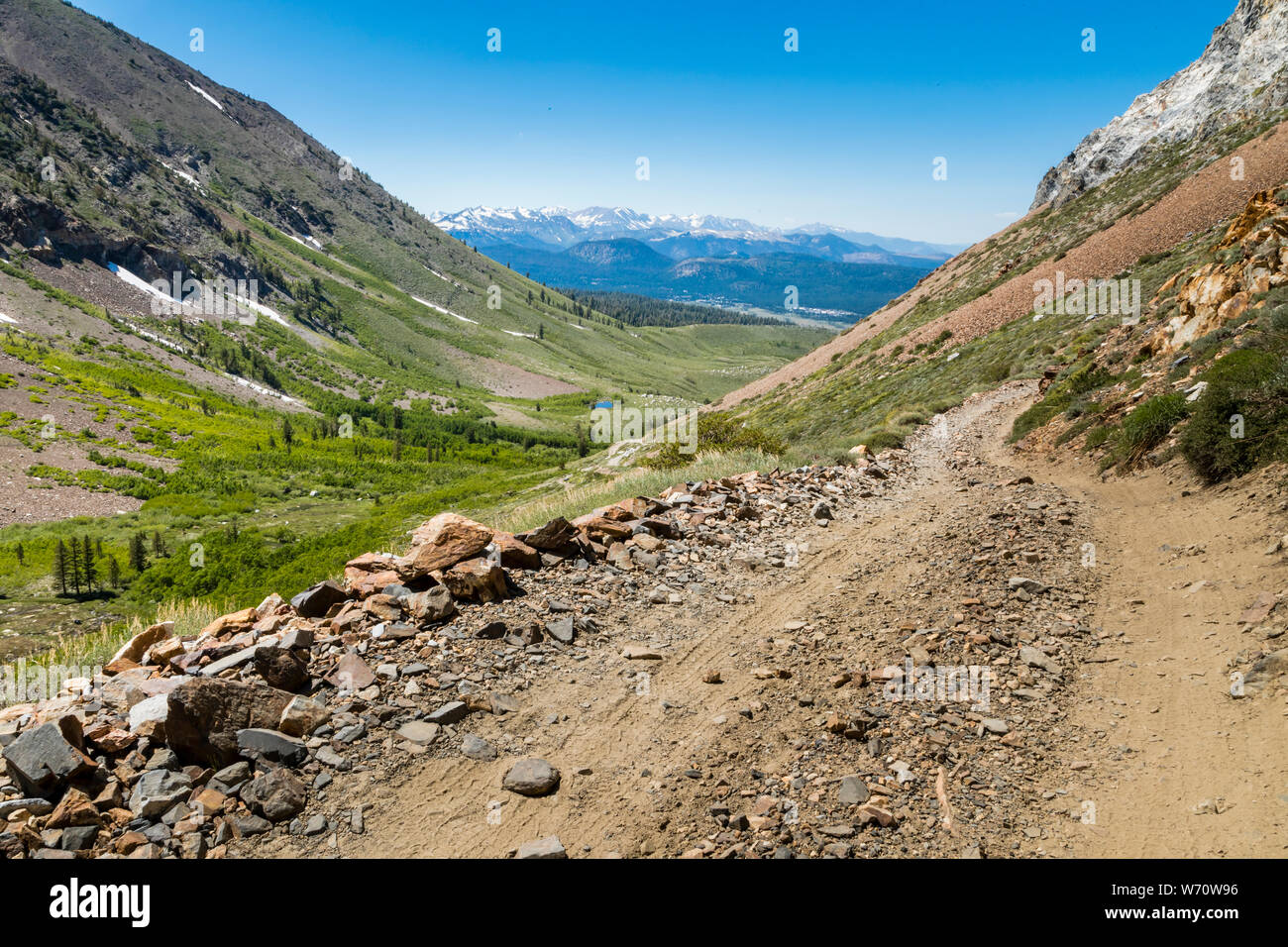 Strada sterrata nella valle verde con prati, montagne e alberi nelle Sierras Foto Stock