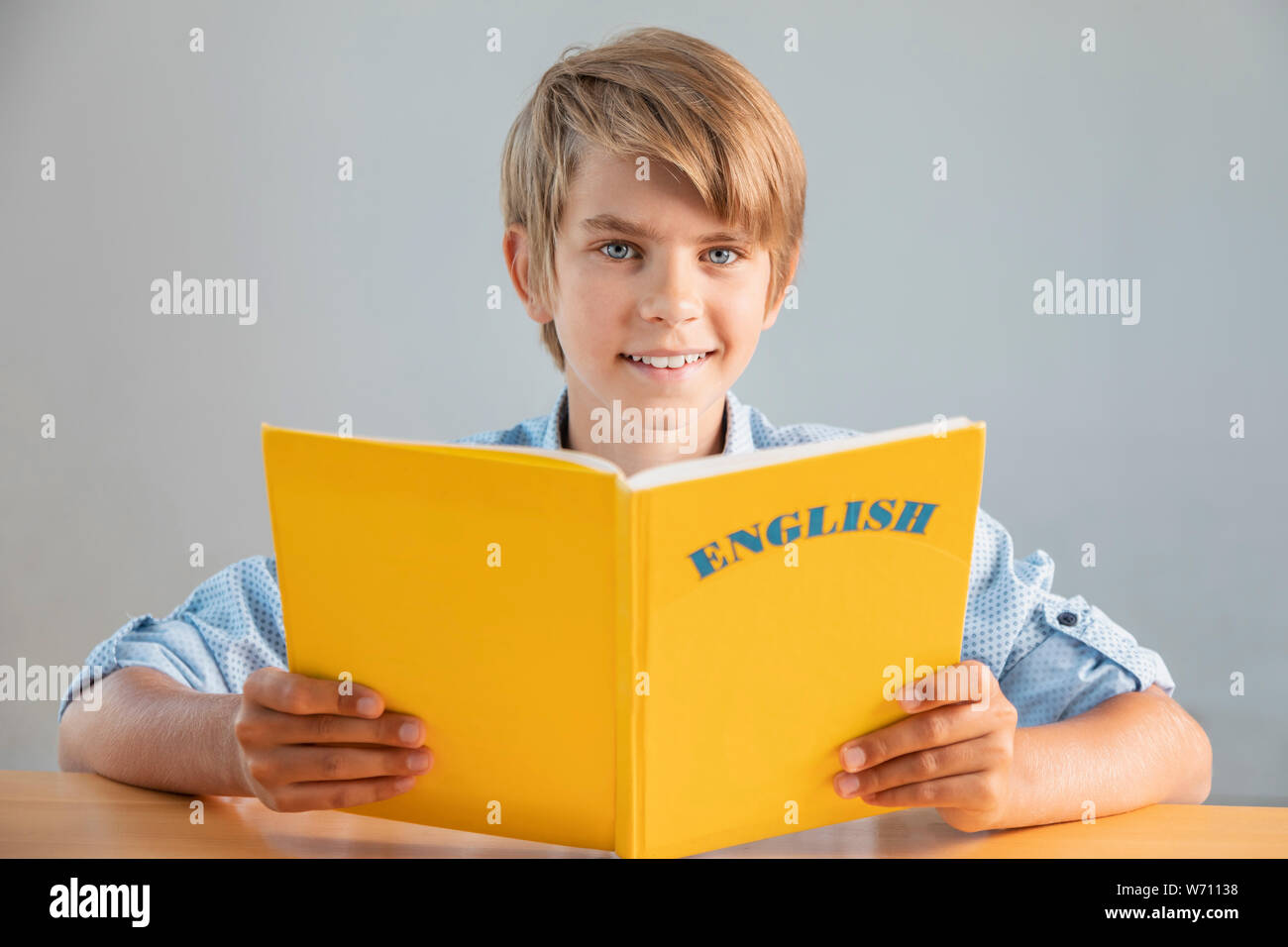 Blonde preteen schoolboy holding giallo libro in inglese Foto Stock