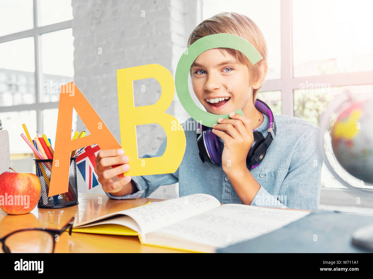 Felice schoolboy gioca con colorate lettere inglesi in ampia classe di luce Foto Stock