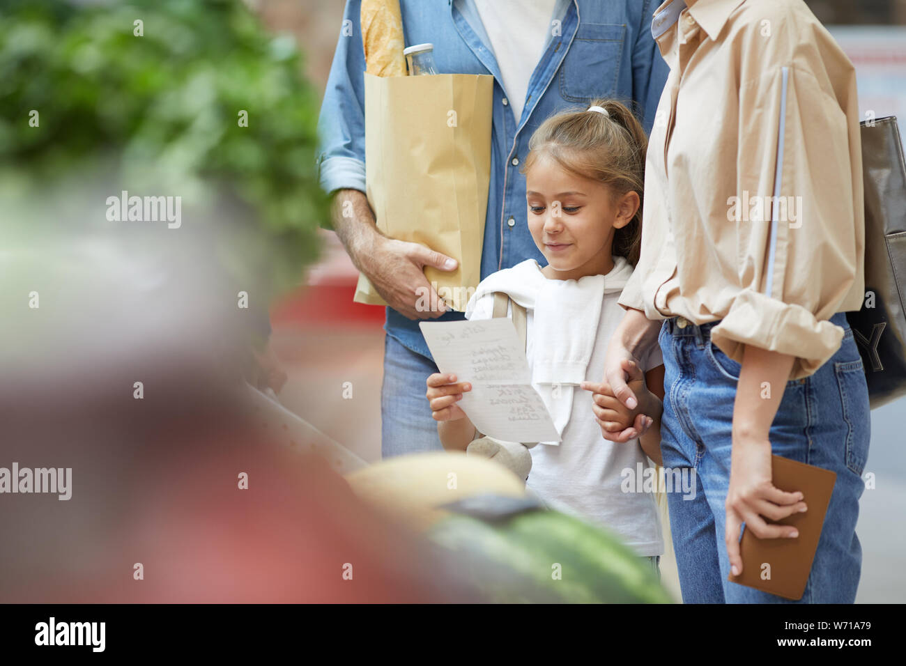 Ritratto di Cute girl carrello con i genitori al mercato degli agricoltori e la lettura della lista della spesa, spazio di copia Foto Stock