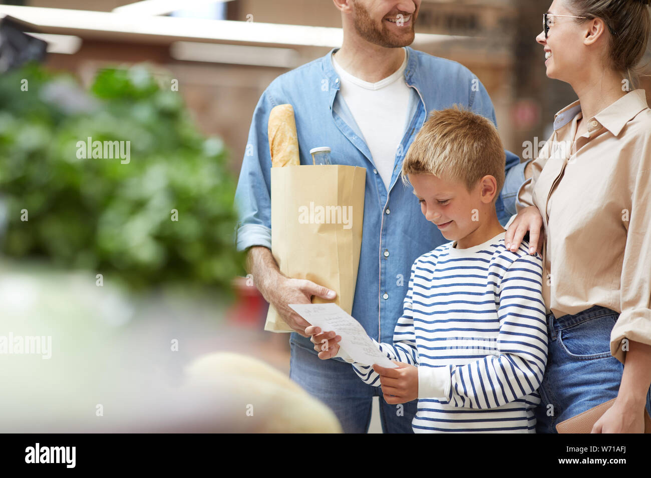 Ritratto di sorridere ragazzo adolescente shopping con i genitori al mercato degli agricoltori e la lettura della lista della spesa, spazio di copia Foto Stock