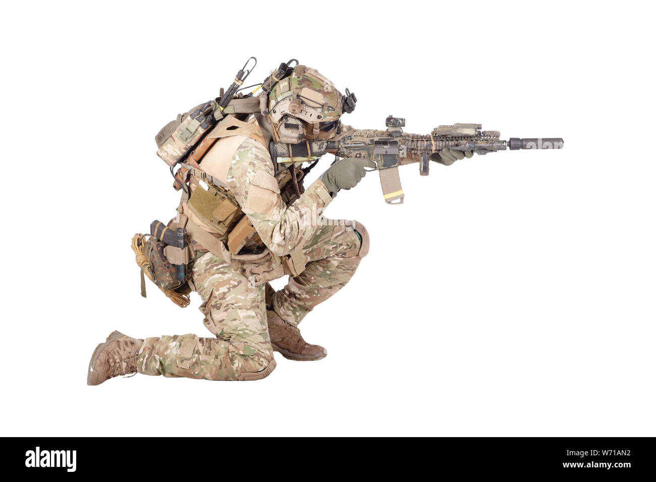 Moderno soldato di fanteria dell'esercito in uniforme da combattimento e casco in piedi sul ginocchio, puntando con la vista laser sul fucile di servizio, sparando in nemico durante le riprese in studio di fuoco isolato su sfondo bianco Foto Stock