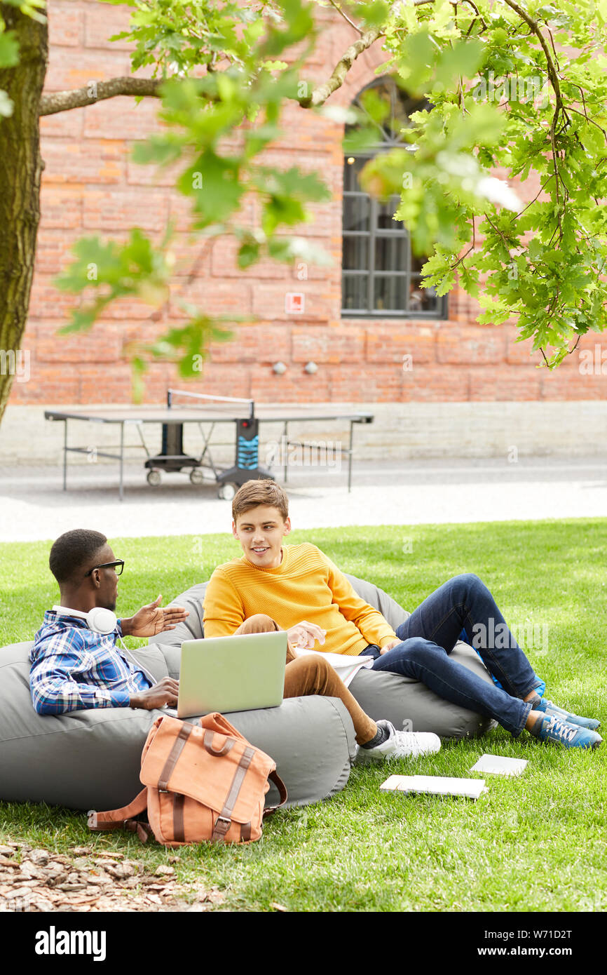 A piena lunghezza ritratto di due studenti di relax all'aperto seduti sui sacchi di fagioli in campus, spazio di copia Foto Stock