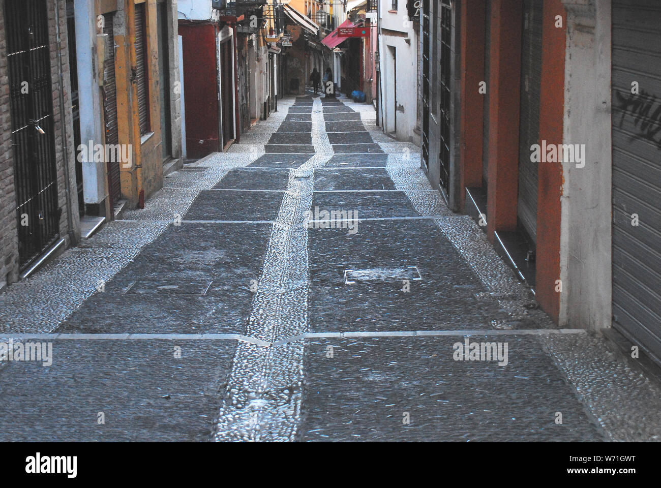 Un wet, strette down hill street foderato con Colorati luminosamente edifici, nel centro della splendida Granada, Spagna. Foto Stock