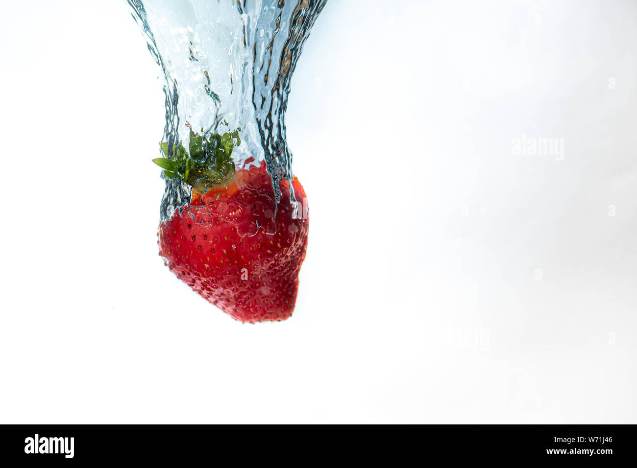 Un singolo strawberry cade in acqua creando una bella bolla di aria come fa. L'acqua si siede su uno sfondo bianco. Non è possibile vedere la superficie Foto Stock