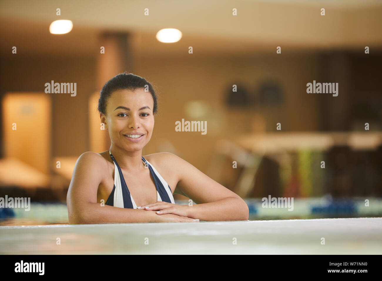 Ritratto di splendida razza mista donna rilassante in piscina e sorridente alla fotocamera, spazio di copia Foto Stock