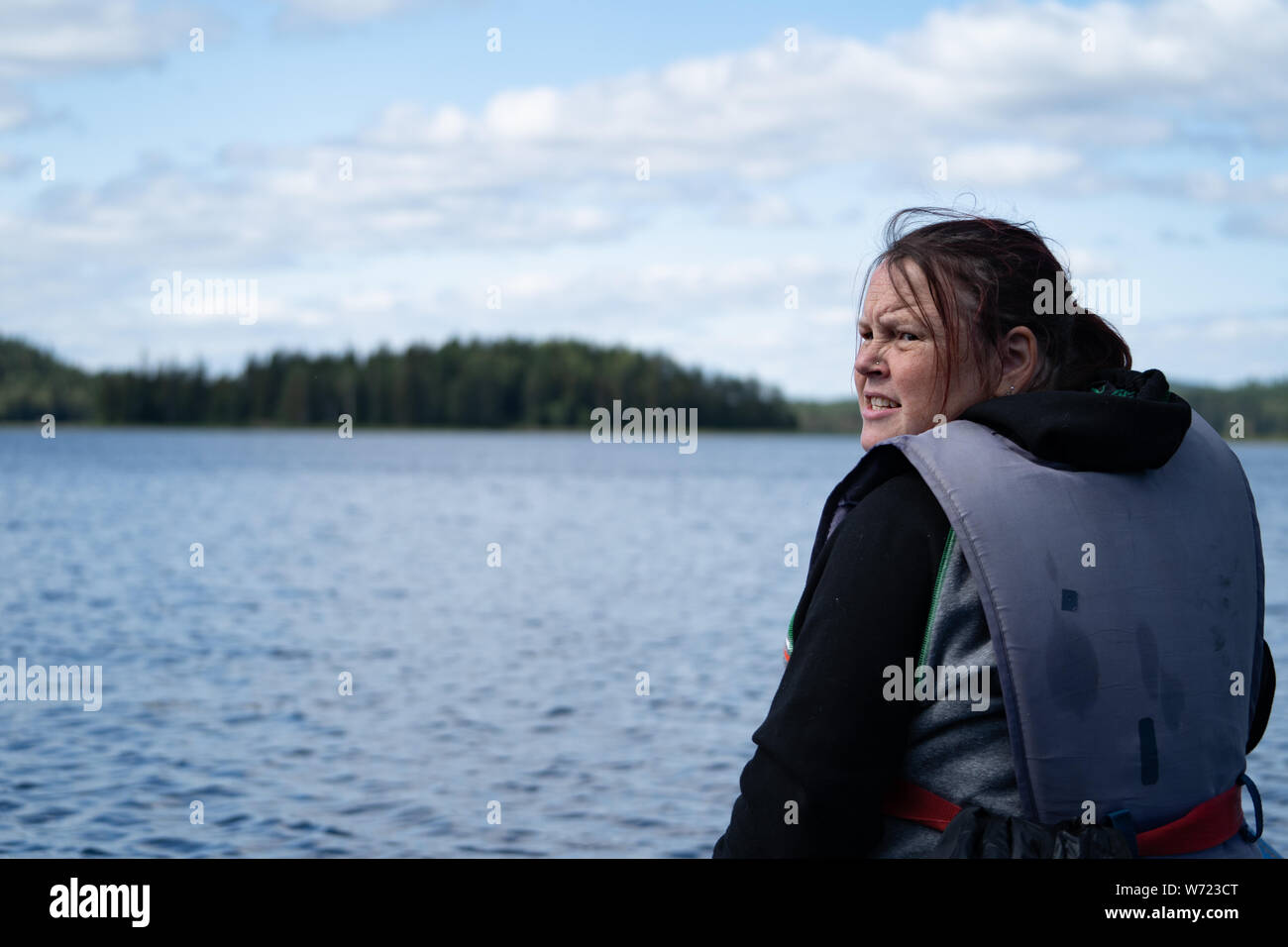 Donna che indossa una spinta di galleggiamento aiuti / giubbotto di salvataggio su un lago (barca non visibile) Foto Stock