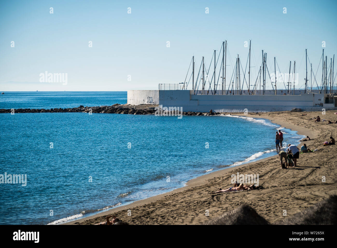 Novembre 21, 2017 - MARBELLA, Spagna. Guardando oltre la spiaggia con le barche in marina dietro. Sole e cielo blu chiaro Foto Stock