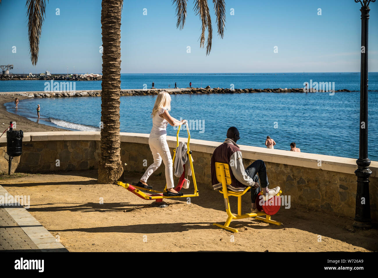 Novembre 21, 2017 - MARBELLA, Spagna. Le persone che usano il pubblico esercizio macchine in una giornata di sole accanto alla spiaggia. Cielo blu e il mare mediterraneo dietro. Foto Stock