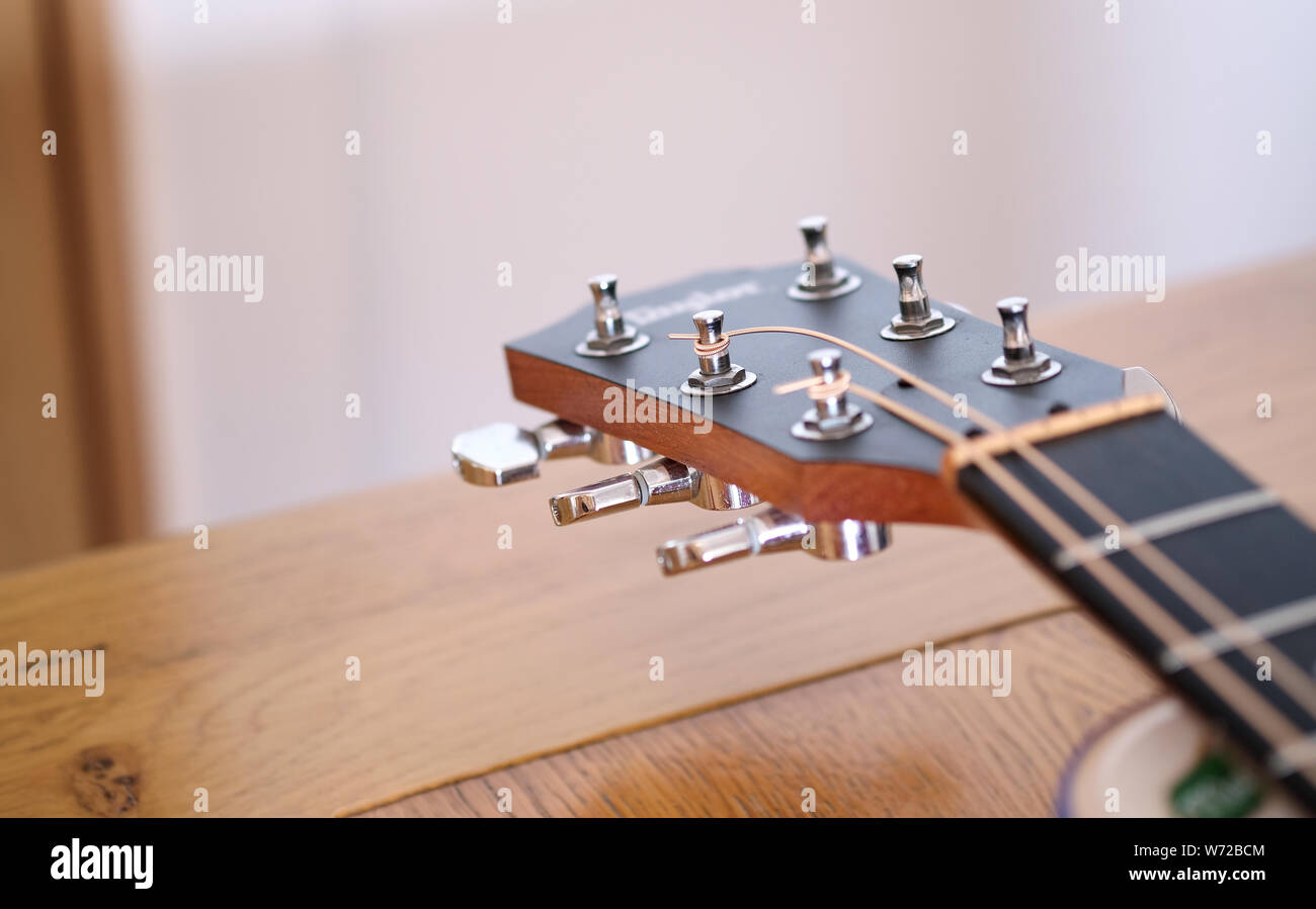 La testa o la parte superiore di un Taylor six string chitarra acustica parzialmente infilate nuovamente con nuove stringhe di acciaio Foto Stock