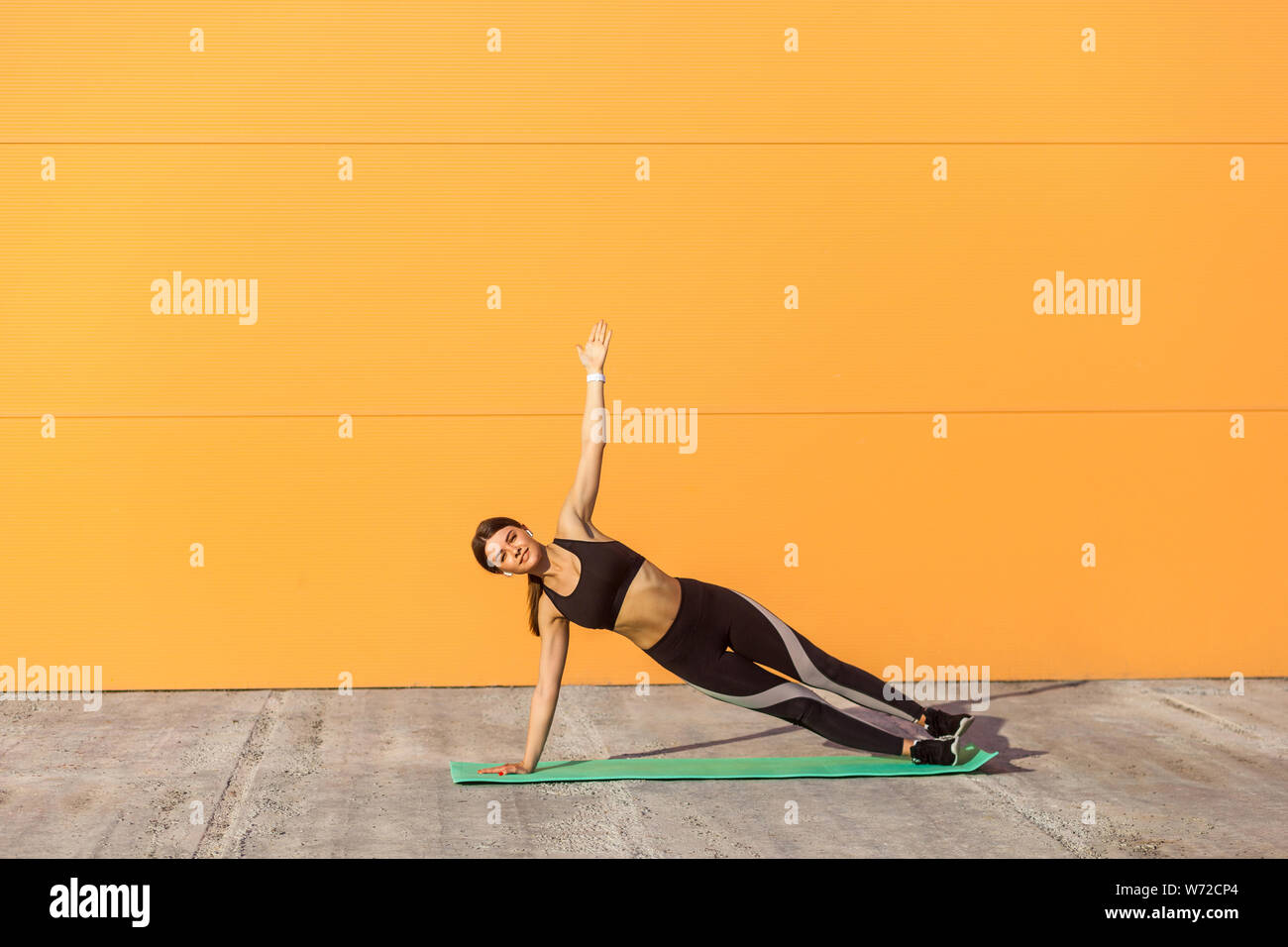 Giovane sportivo da donna attraente la pratica dello yoga, facendo esercizio vasisthasana, laterale plank pongono, lavorando sul tappeto verde, indossare abbigliamento sportivo nero, superarsi Foto Stock