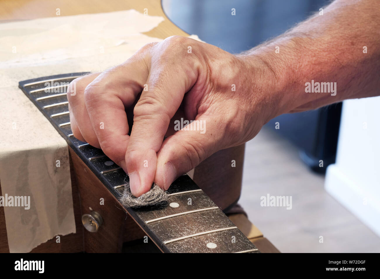 Una chitarra acustica essendo sottoposto a manutenzione. Il tecnico è la pulizia della tastiera con fine filo di lana Foto Stock