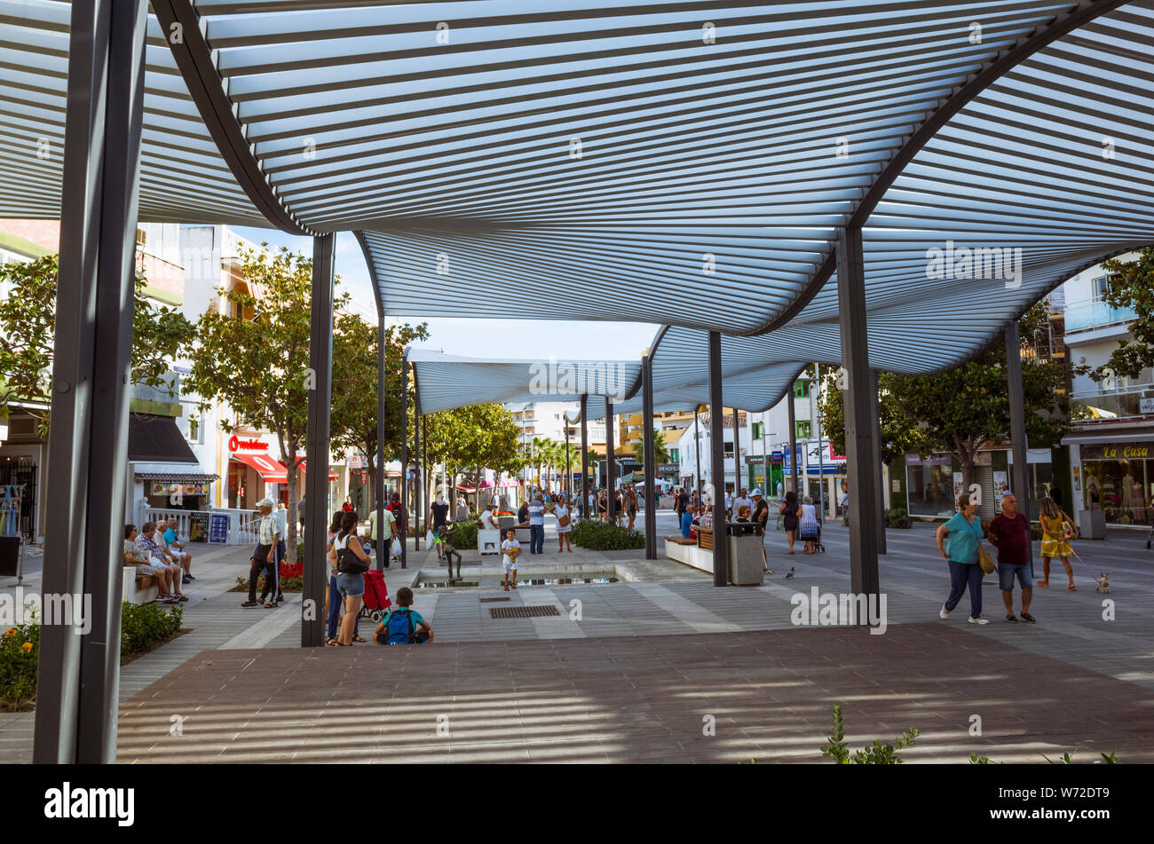 Torremolinos, provincia di Malaga, Andalusia, Spagna - Giugno 19th, 2019 : la gente a piedi sotto gli ombrelloni presso la Costa del Sol quadrato al centro della torre Foto Stock