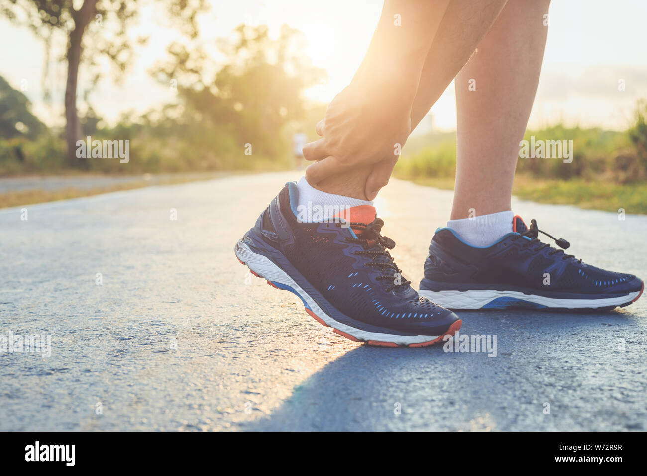 Pregiudizio dal concetto di allenamento : l'uomo asiatico di usare le mani tenere su la sua caviglia durante il funzionamento su strada nel parco. Focus sulla caviglia. Foto Stock