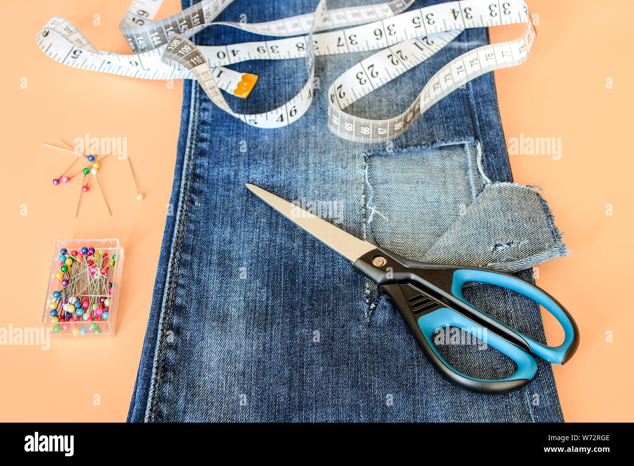 Jeans blu con foro grande piegato a metà, perni di cucitura in una casella bianca del nastro su misura con centimetri e pollici e forbici. Accorciare i jeans. DIY sh Foto Stock