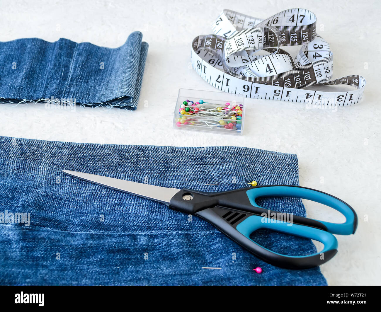 Rendendo shorts in jeans blu con multi colore cucitura testa perni, bianco nastro su misura con centimetri e pollici e forbici. Accorciare i jeans. Foto Stock