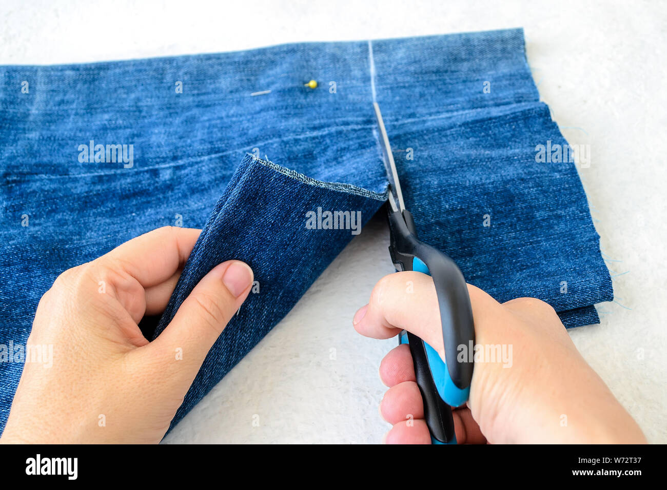 Donna mano trattiene un forbici e il taglio di una piegato a metà blu jean corti. Accorciare il denim shorts con forbici e la cucitura di pin. Accorciare un paio di jeans Foto Stock