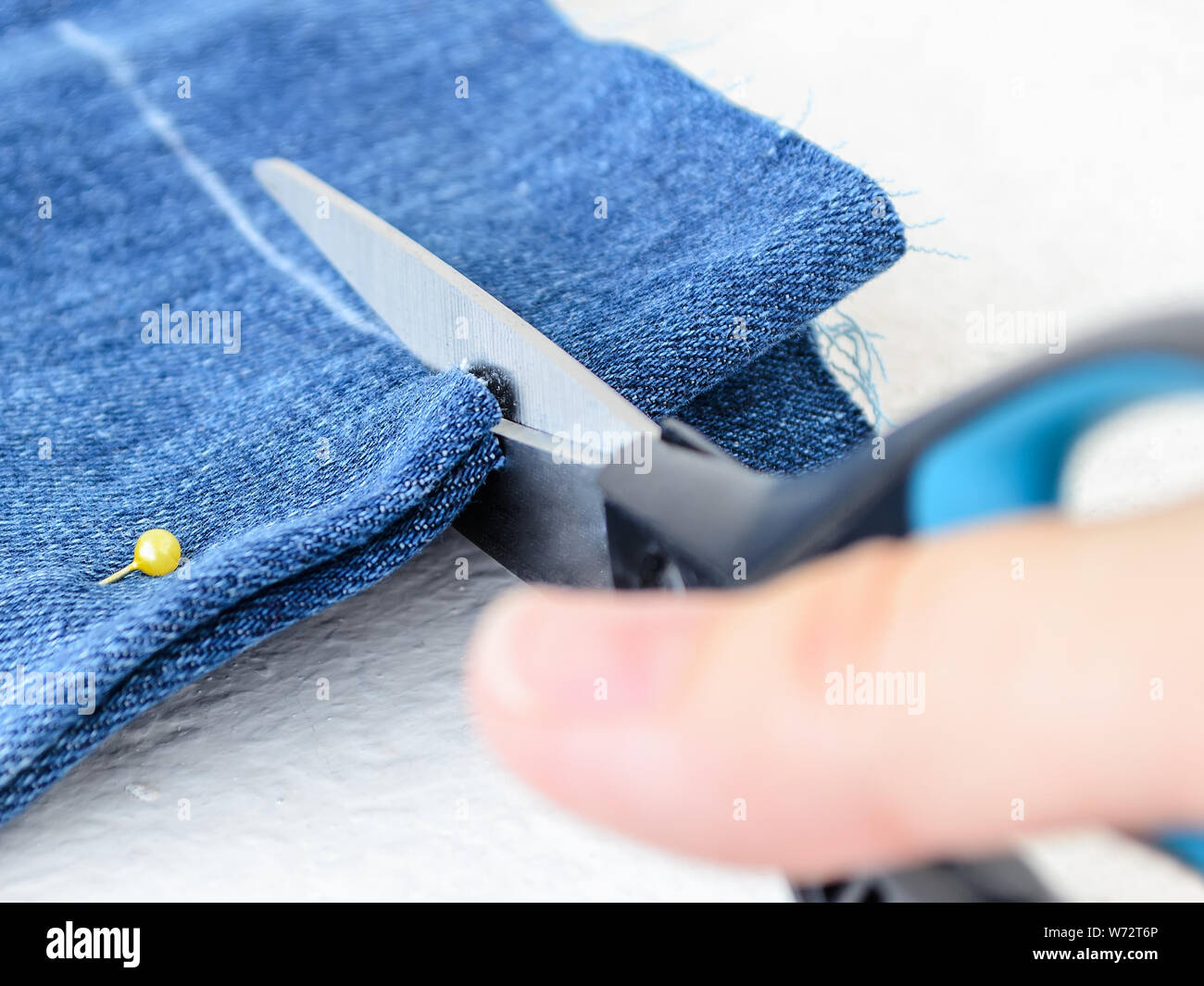 Close-up di donna mano che tiene una forbice e taglio piegato a metà blu jean corti. Accorciare il denim shorts con forbici e testa di colore Foto Stock