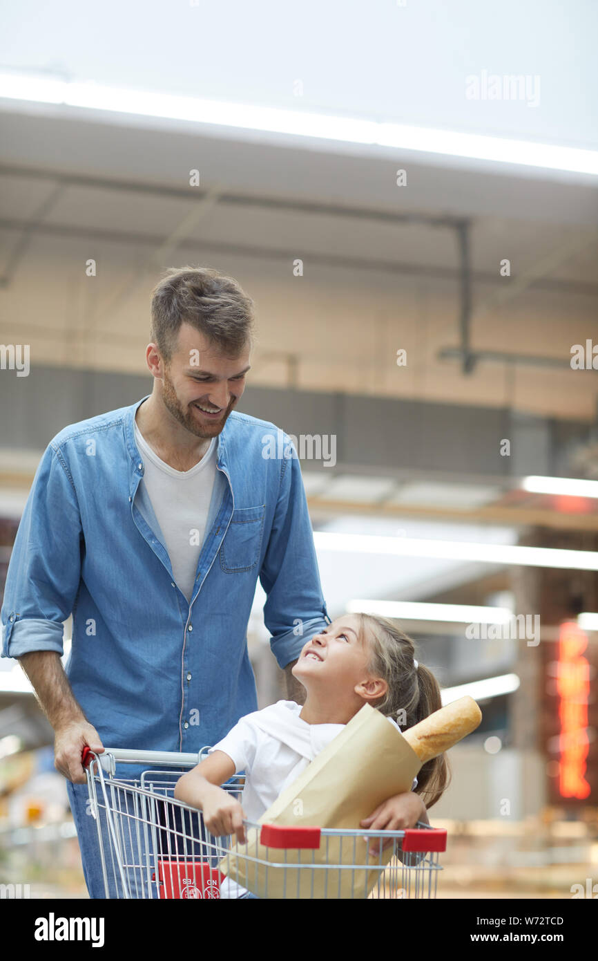Ritratto di felice giovane padre a fare la spesa nel supermercato e sorridente a poco ragazza seduta nel carrello Foto Stock