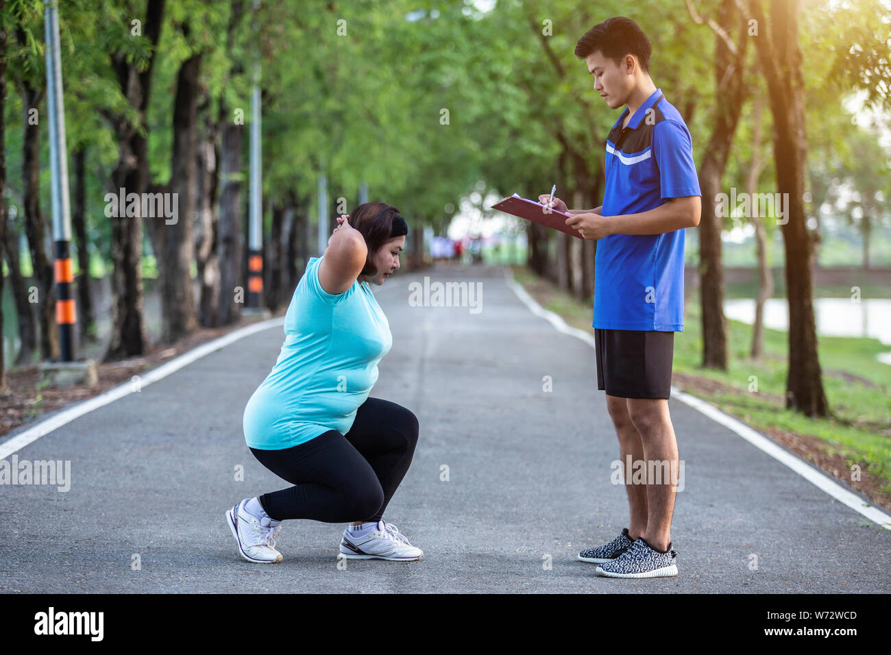 Uomo asiatico scrittura su carta nella parte anteriore del grasso donne mentre facendo scot jump nel parco Foto Stock