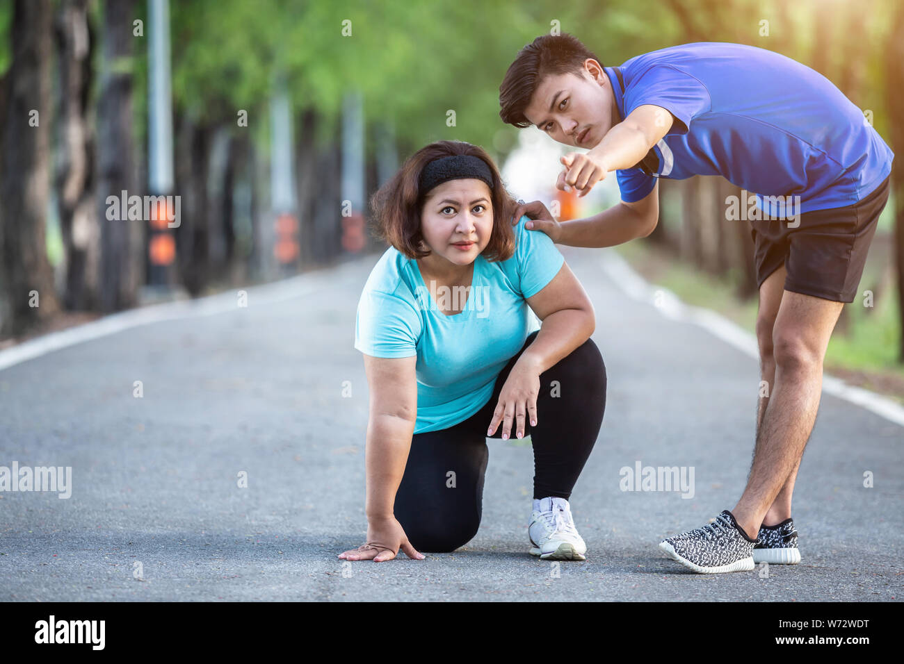 Uomo asiatico rendono incoraggiamento alla donna grassa che seduto sul terreno e punto la sua mano per il bersaglio Foto Stock