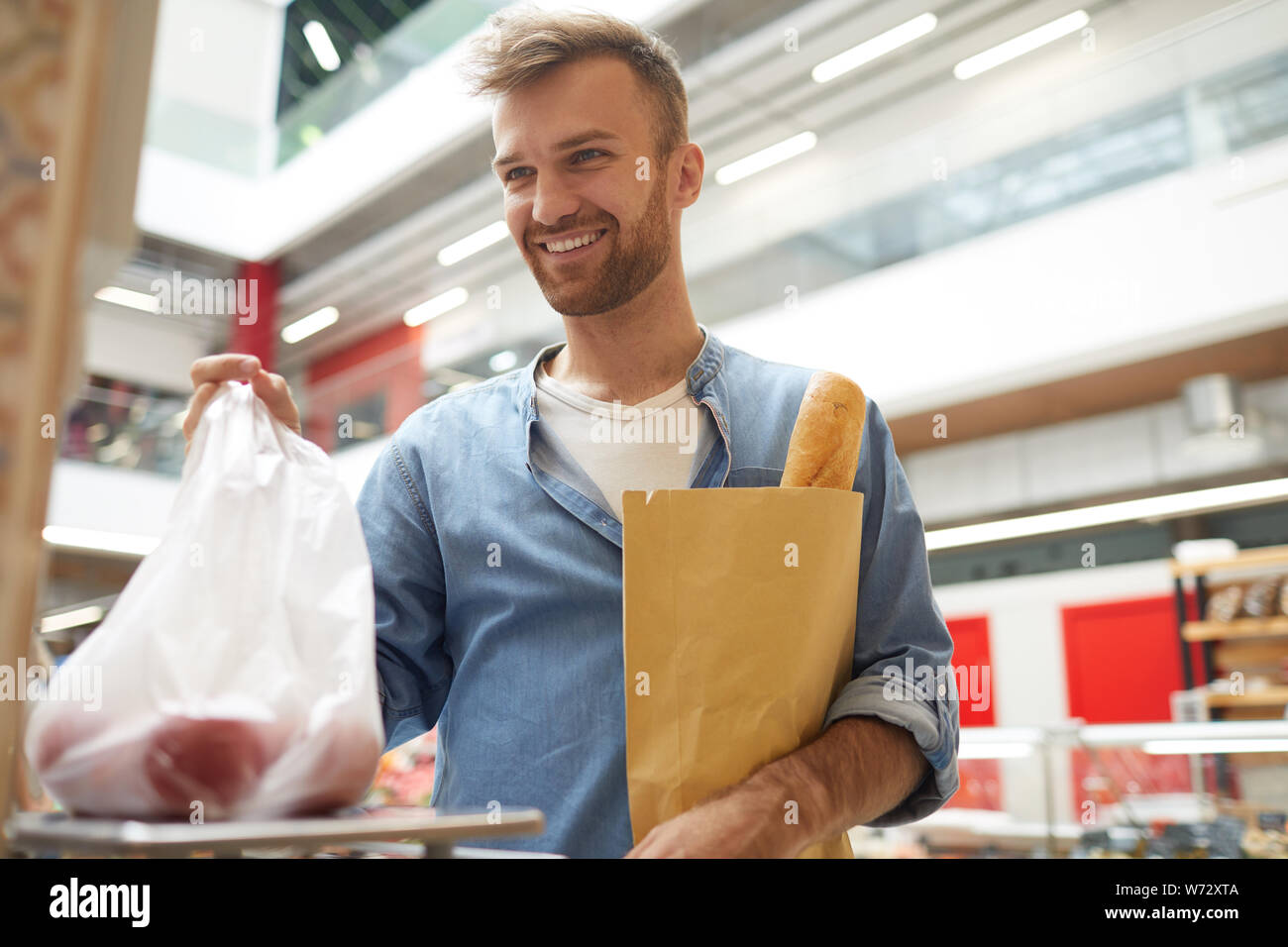 Vita ritratto di bel giovane del peso di verdure nel supermercato e sorridente al cassiere, spazio di copia Foto Stock