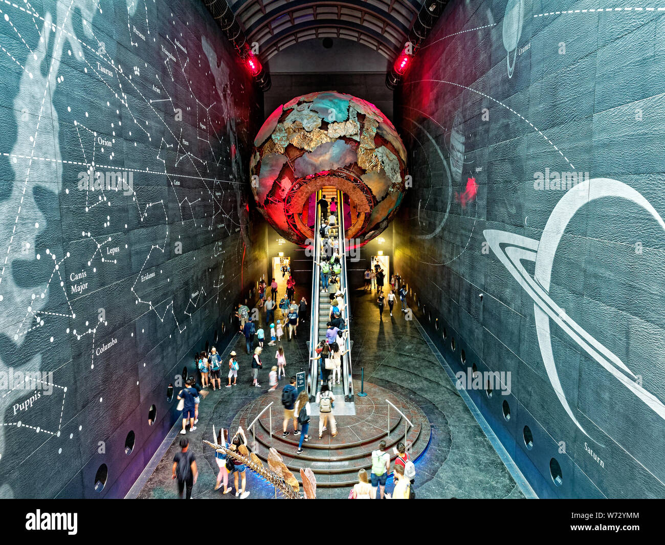 La folla di turisti che viaggiano su una scala mobile passando attraverso un globo di metallo in terra Hall presso il Museo di Storia Naturale di Londra Foto Stock