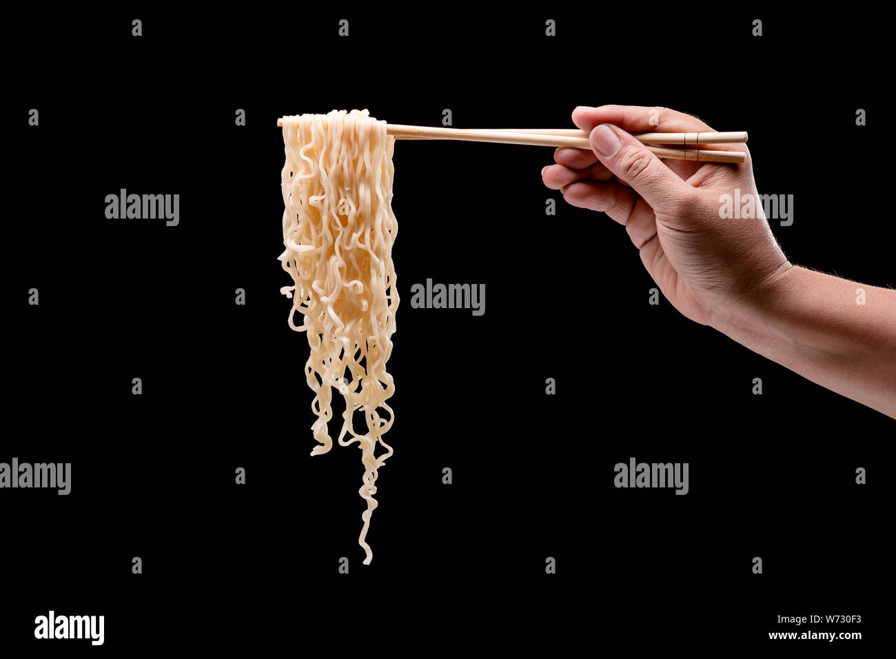 Mano che tiene le bacchette di bambù e la forcella più tagliatelle istante. Studio shot isolato su sfondo nero Foto Stock