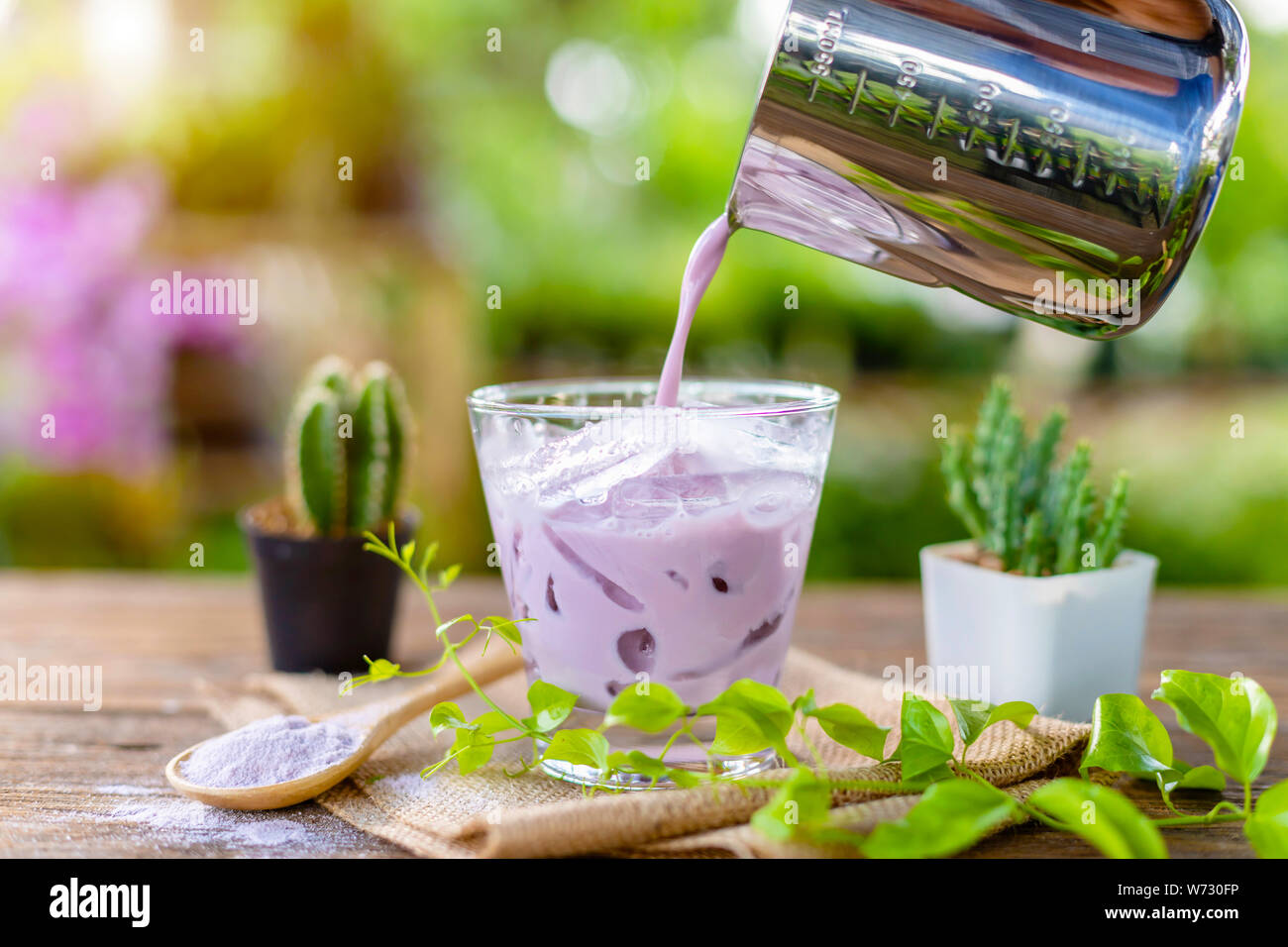 Iced viola Taro il latte in vetro chiaro servita su un tavolo di legno in un garden cafe'. Ghiaccio concetto di menu Foto Stock