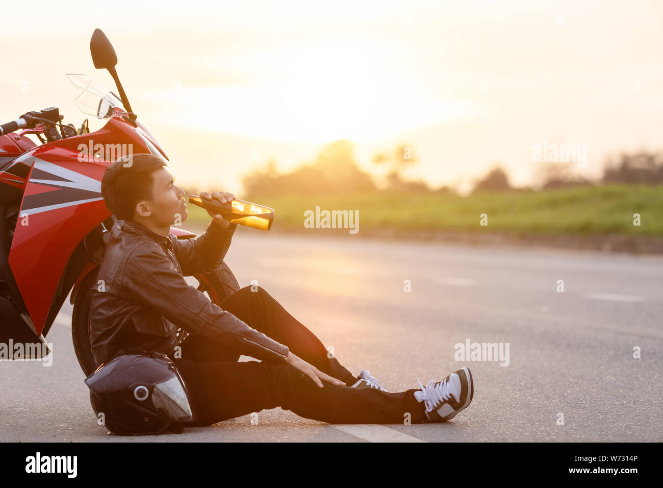 Motociclista seduto sulla strada accanto alla sua moto e bere un alcol o birra. Di sicuro ride concept Foto Stock