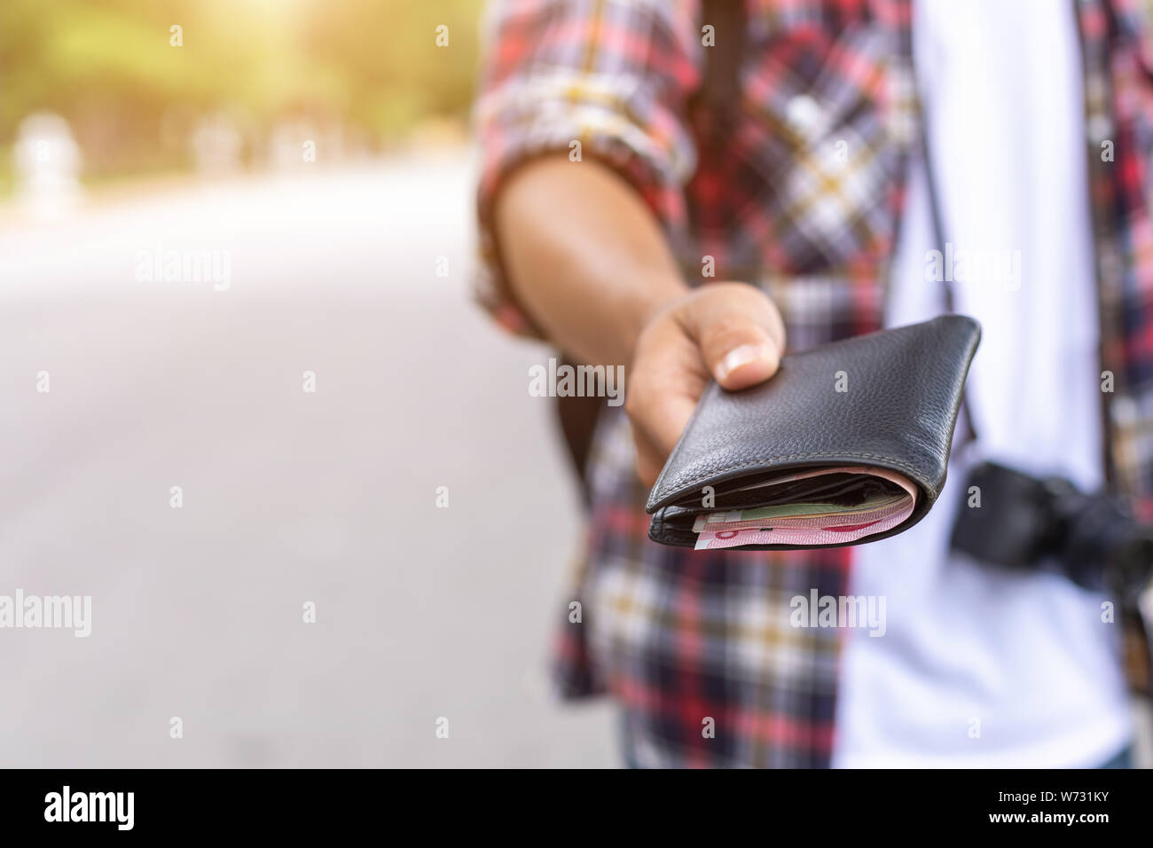 Mano di turisti asiatici dando la banconota e portafoglio nero che ha trovato in attrazione turistica. Perdere il concetto di portafoglio Foto Stock