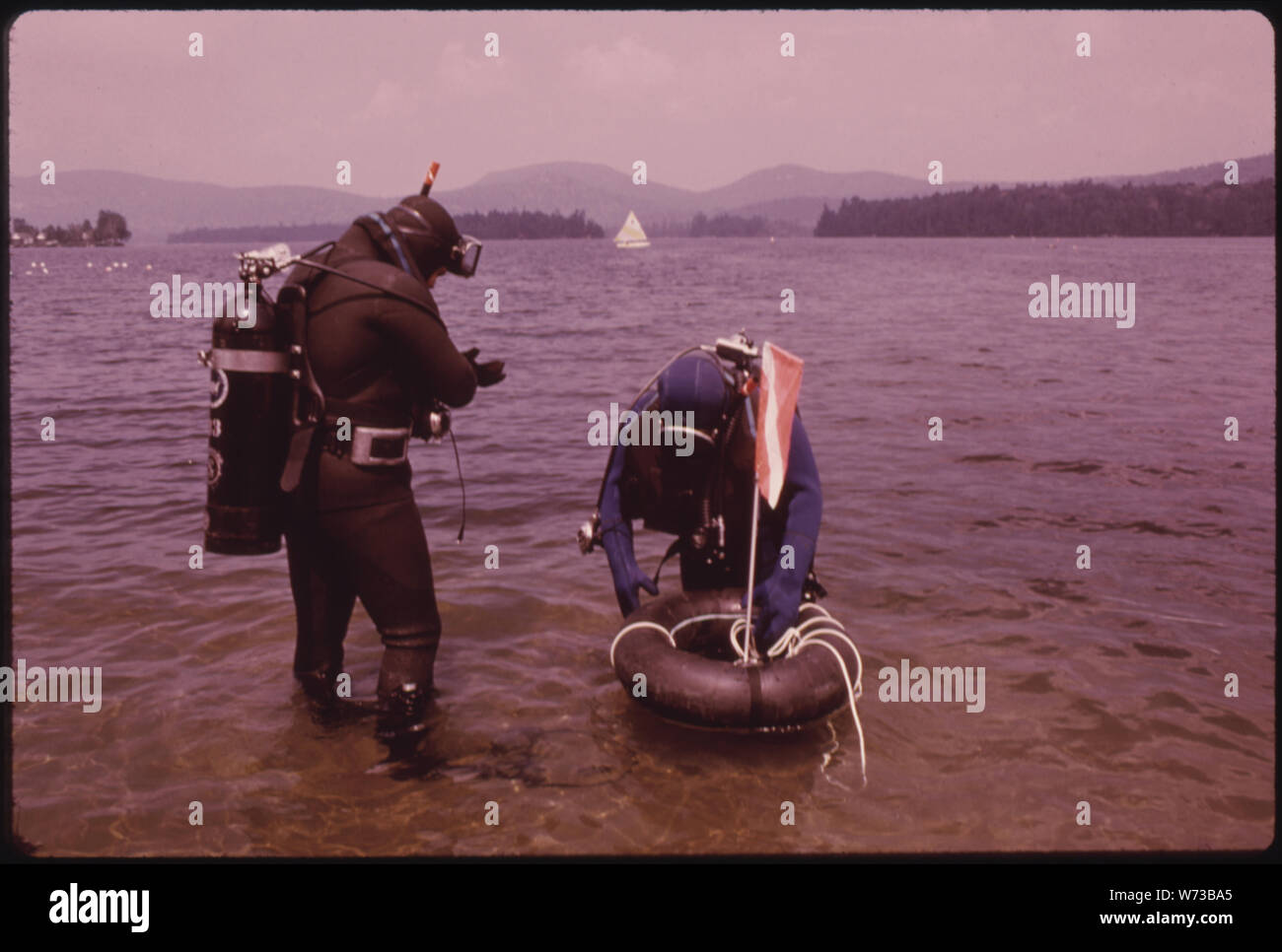 Due subacquei DA UNA NEW YORK CITY CLUB PRONTO IL LORO TUBO DI SICUREZZA CON bandiera che galleggia sopra la loro area immersioni per avvertire i barcaioli. I subacquei sono alla ricerca di barche affondata, vaporizzatori e vagoni ferroviari in BLUE MOUNTAIN LAKE IN ADIRONDACK Forest Preserve Foto Stock