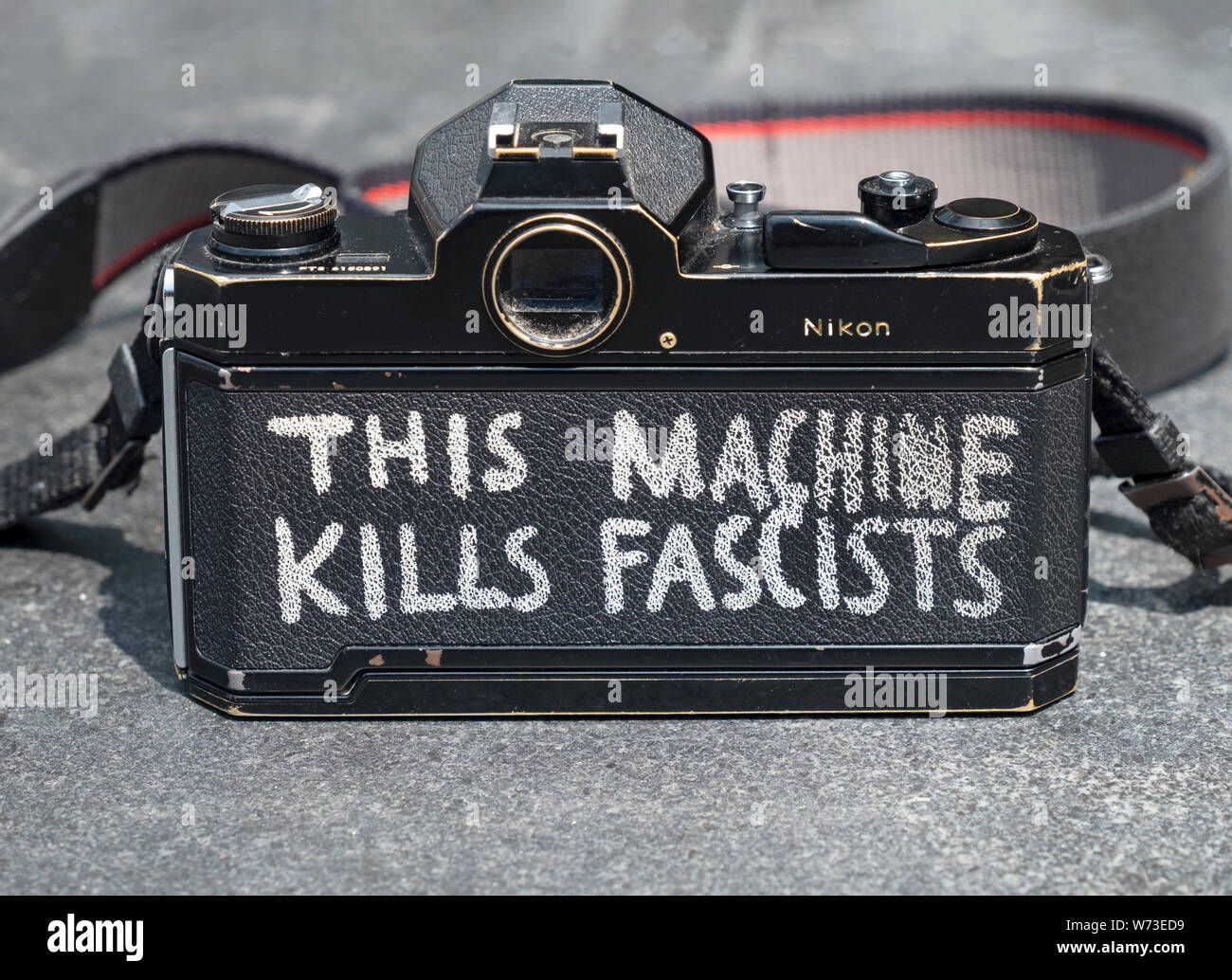 Questa macchina uccide i fascisti. Un fotografo dipinto di Woody Guthrie slogan sul retro della sua Nikon fotocamera a pellicola. In Washington Square Park di New York. Foto Stock